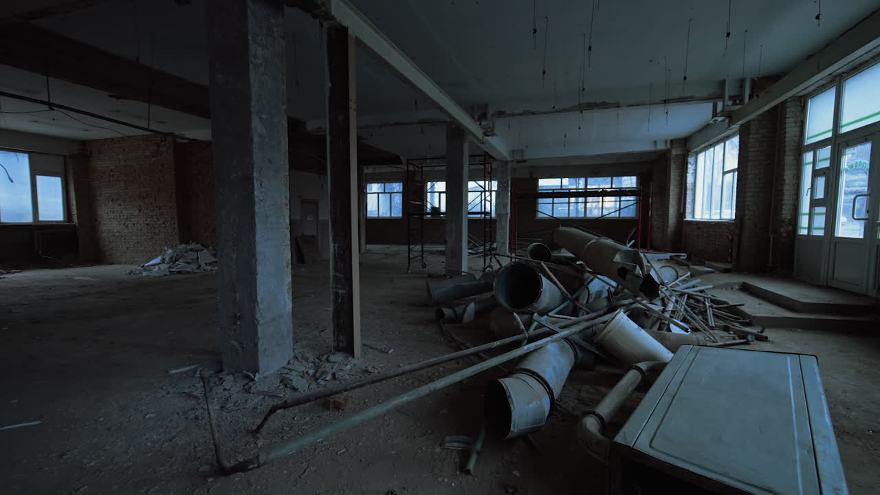 Interior of a big spacious room with shabby walls, columns and large windows. Old ventilation pipes are in a pile on the floor.