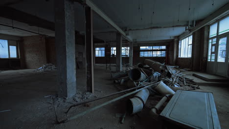 interior of a big spacious room with shabby walls, columns and large windows. old ventilation pipes are in a pile on the floor.