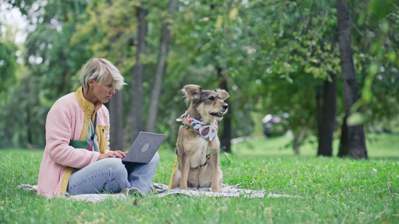 Woman Working on Laptop while Sitting Next to Dog in City Park