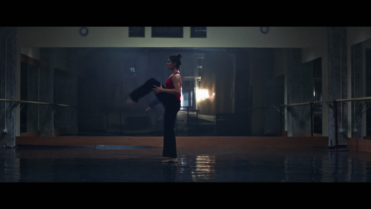 A young woman practices modern dancing and ballet in a moody room full of mirrors