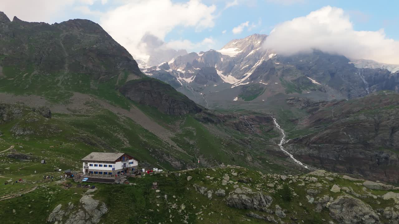 Panoramica aerea da sinistra del ghiacciaio della Fellaria con un rifugio alpino circondato da cime rocciose e terreno alpino