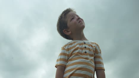 a child looks up to the sky with a dreamy expression, symbolizing curiosity, hope, and the search for meaning, watching the clouds.