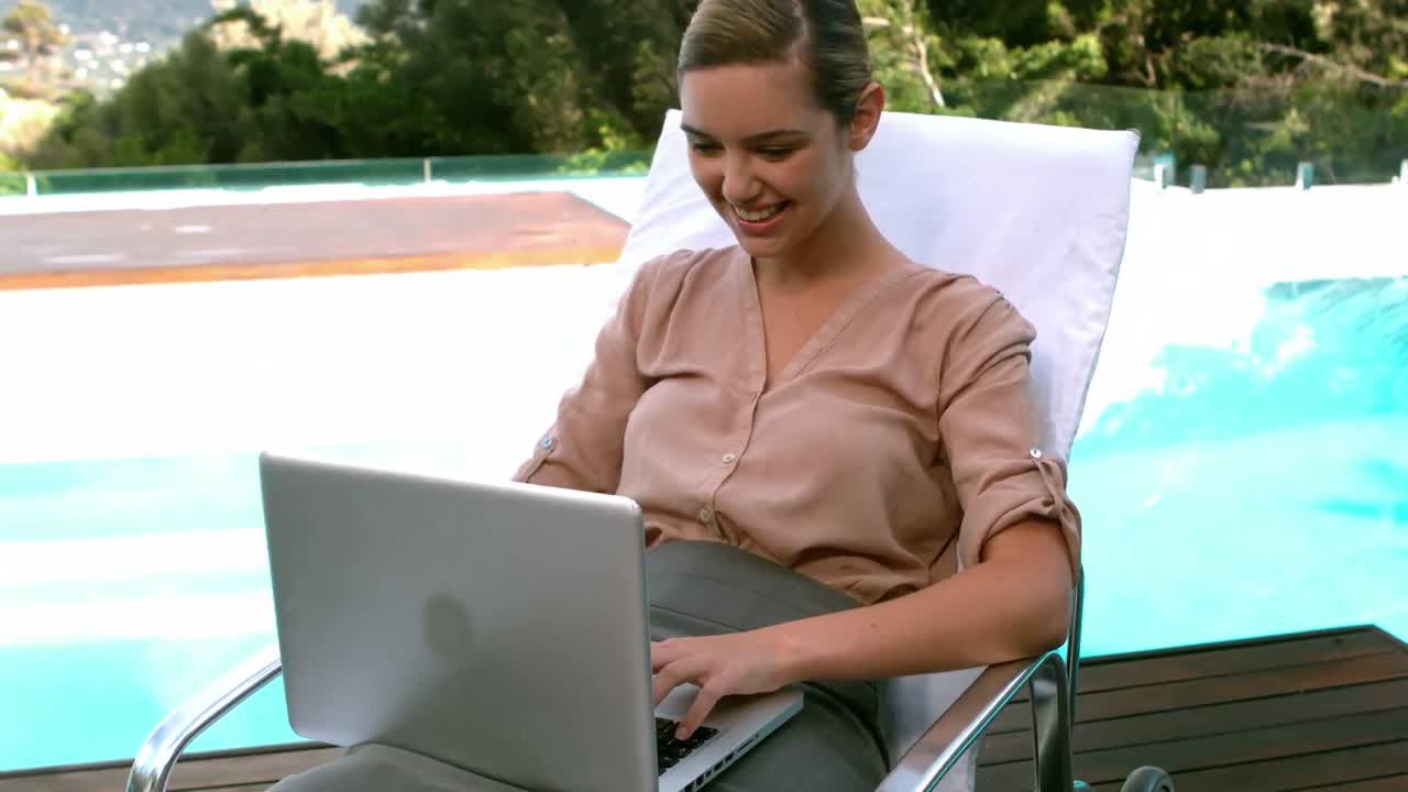 una mujer de negocios sonriente usando una computadora portátil junto a la piscina.
