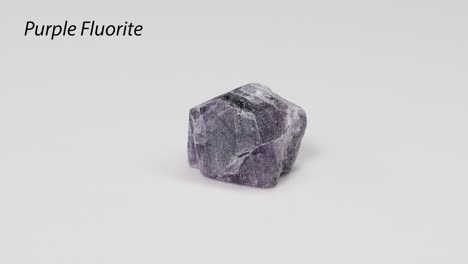 a purple fluorite crystal rotating on a white surface.