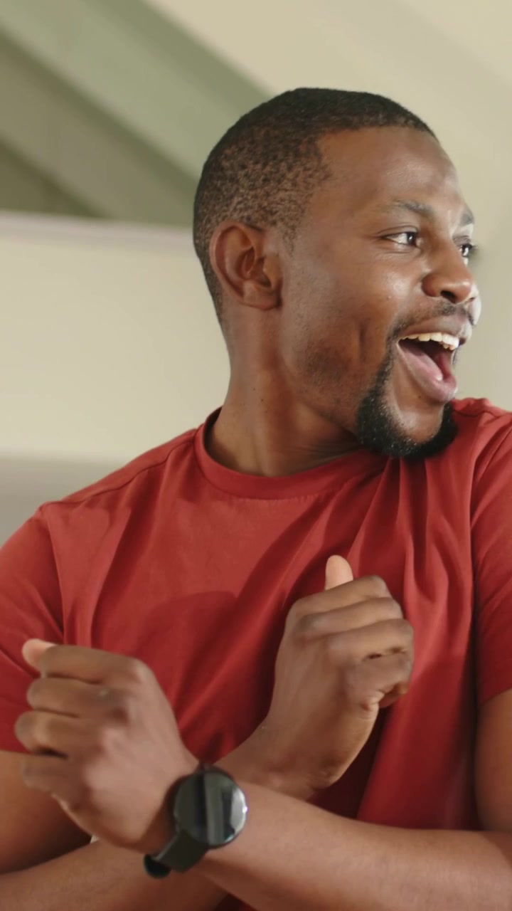 Vertical video: Orange arm appearing, man red tee turning right on couch, smiling and showing watch