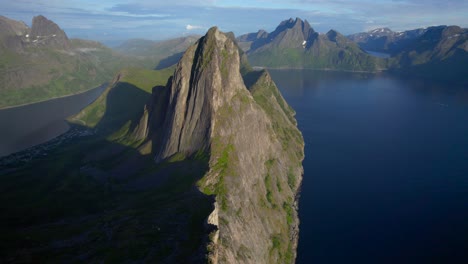 Toma-Aérea-De-Avance-De-La-Espectacular-Montaña-Segla-Con-Su-Acantilado-En-El-Borde-Del-Mar-Y-Montañas-Angulares-Al-Fondo,