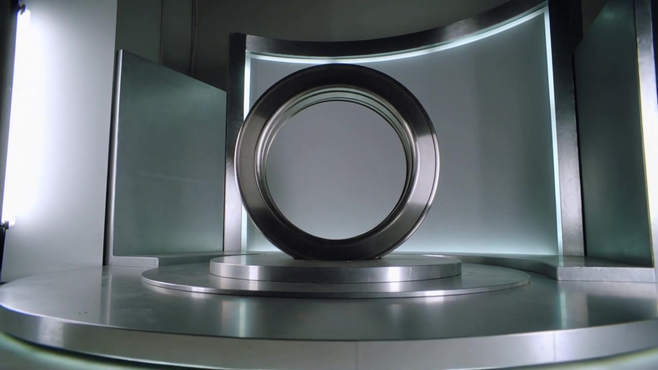 Kameraet trækker sig tilbage og viser en stor metalring oprejst på en roterende scene til en produktlancering.