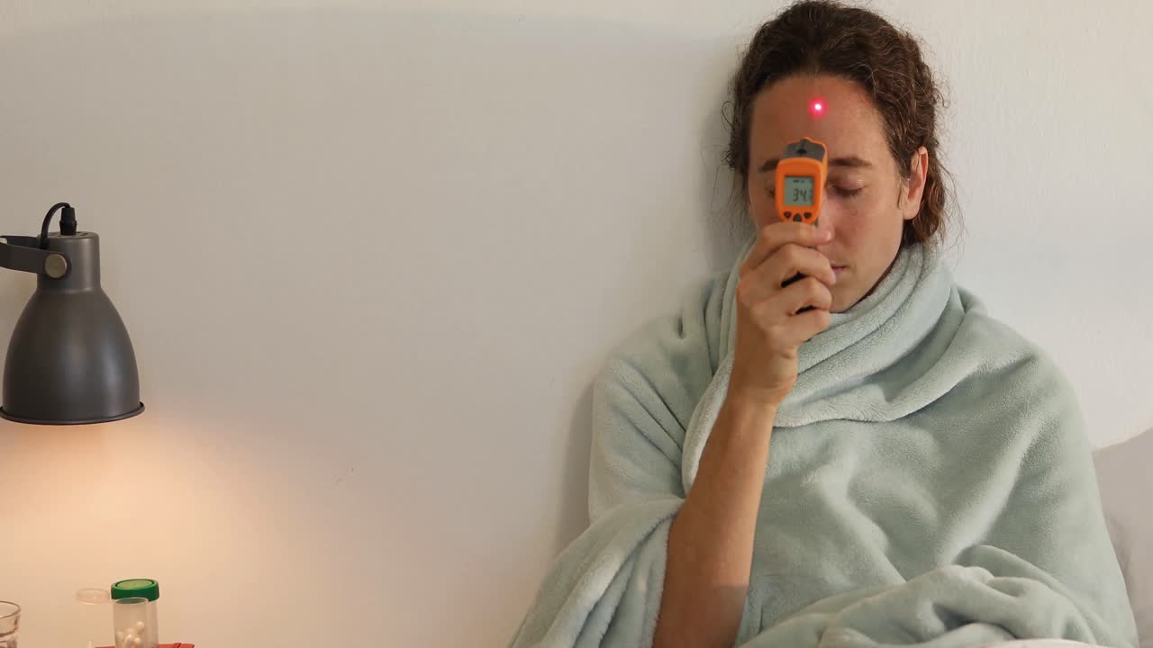 mujer caucásica enferma tomando su temperatura en casa