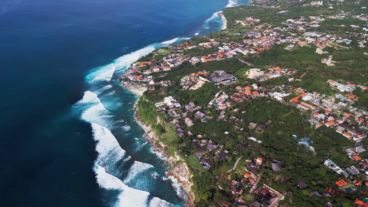 Drone view of a striking coastal cliff where turquoise waves break against rough stone walls, highlighting dramatic textures, sweeping shoreline curves, and the intense natural power of the open ocean