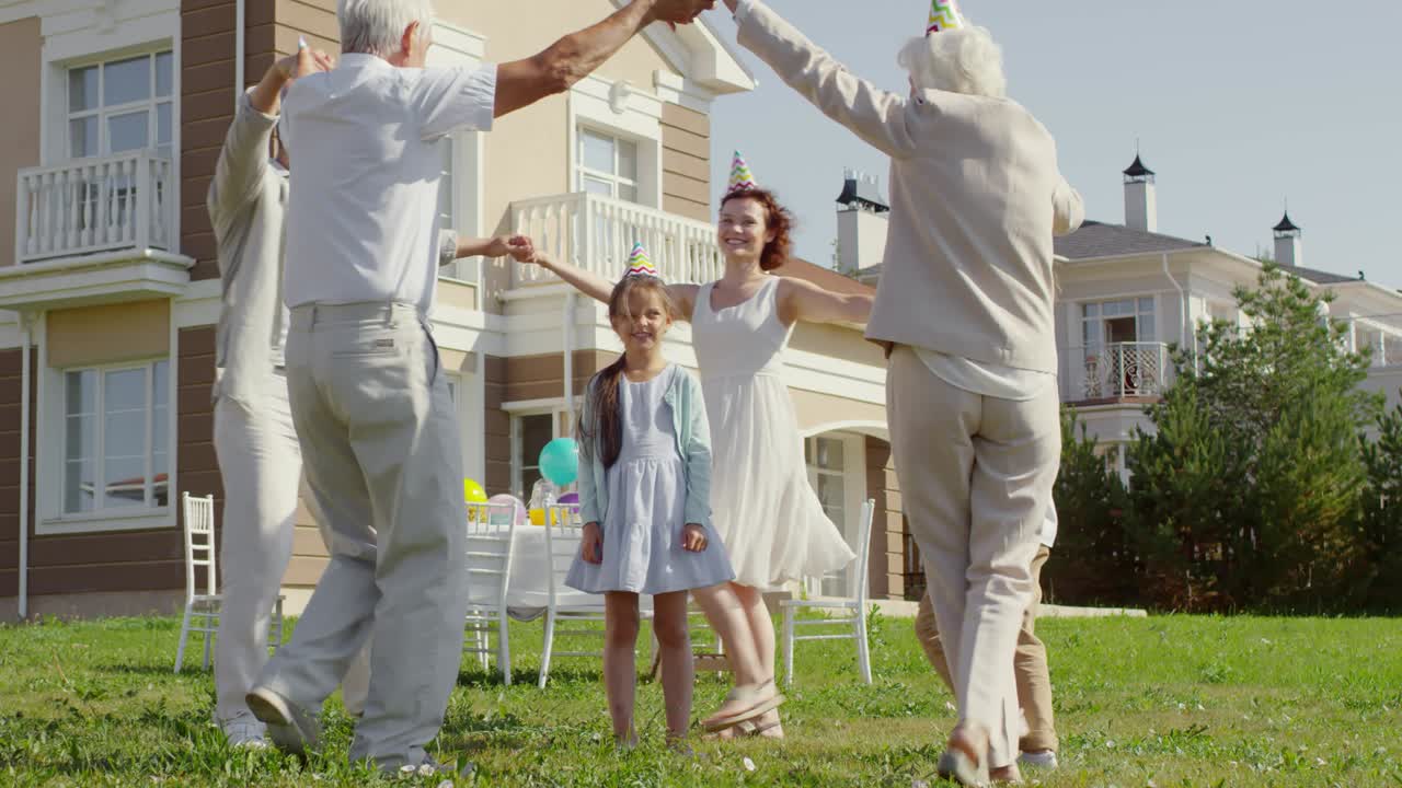 feliz familia bailando alrededor de la niña de cumpleaños al aire libre