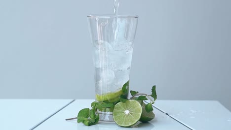 water pours into glass with ice cubes and lime slice inside