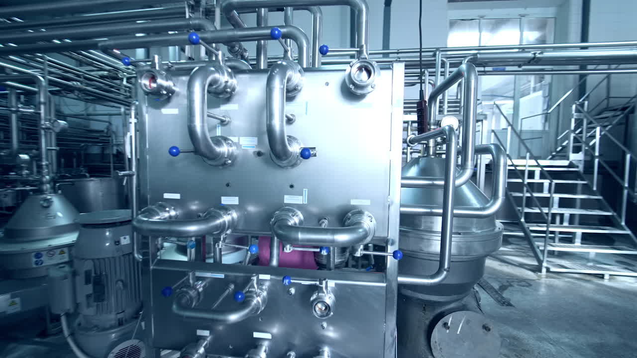 Steel shining pipes and milk tanks at modern dairy plant. Factory female worker in special uniform standing among the industrial equipment.