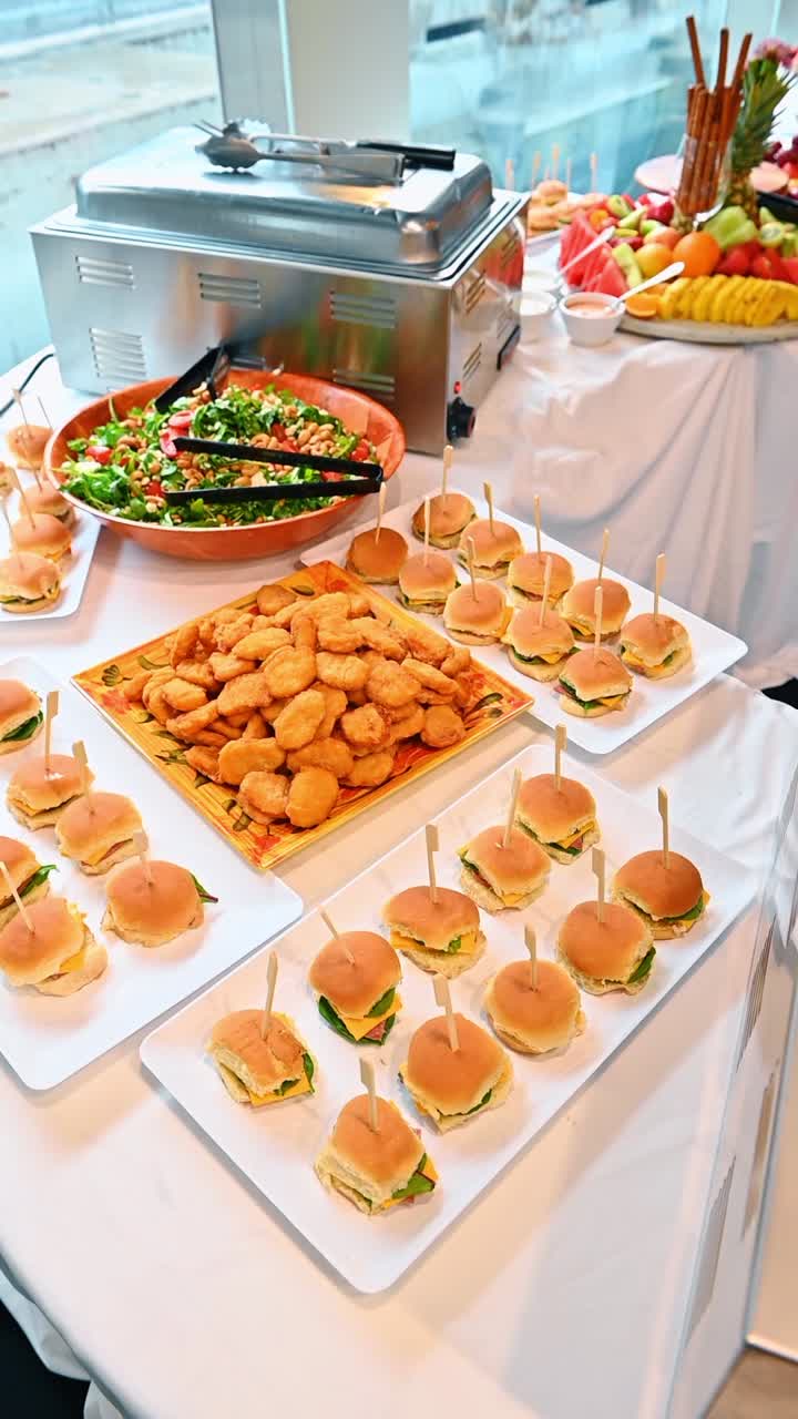 Selezione di crocchette di pollo e mini-hamburger sul buffet. Piatti bianchi con mini-hamburger, un vassoio di crocchette di pollo dorate e insalata fresca in una ciotola.