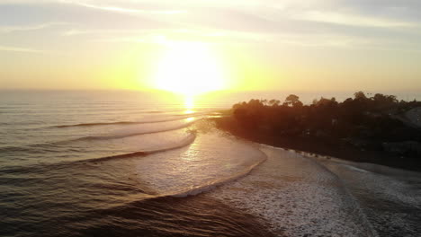 aerial drone shot over rincon point surf break with ocean waves and surfers riding during sunset on the beautiful california coastline