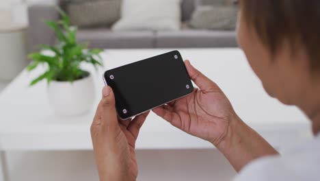 African-american-senior-woman-sitting-on-couch-using-smartphone,-with-copy-space-on-screen