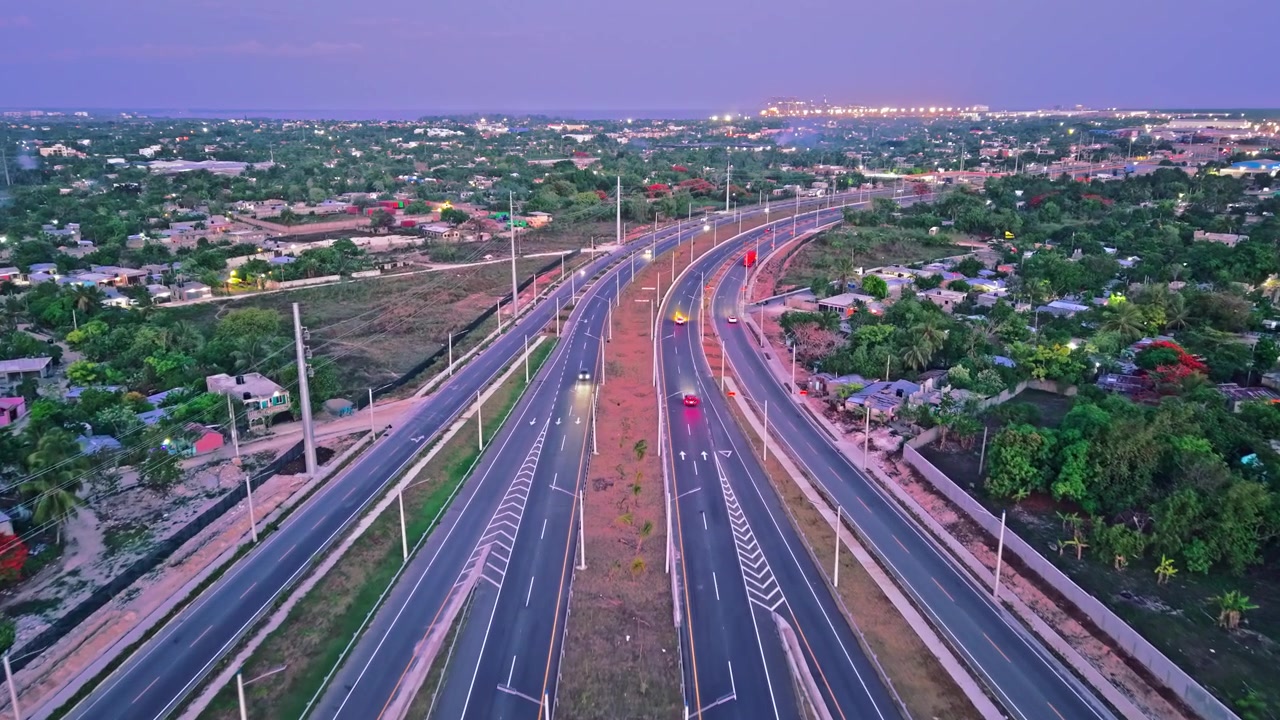 High-angle aerial drone shot flying forward over a curved multi-lane highway at dusk, capturing vehicle traffic driving on paved lanes under a purple twilight sky