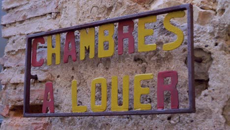 Cartel-De-Metal-En-Una-Pared-De-Piedra-Que-Indica-Habitaciones-En-Alquiler-O-Chambres-À-Louer-En-Francés-En-Cámara-Lenta-En-Pueblo-Provenzal