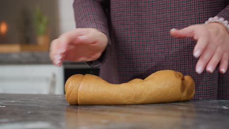 partial view of chef with bracelet on left hand adjusting and kneading fresh dough on kitchen counter, preparing homemade baked goods in modern kitchen with warm lighting and sleek appliances