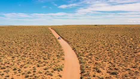 One-SUV-car-travelling-along-the-countryside-dirt-road-in-Utah-desert---aerial-revealing-takeoff-back-view-shot-,-Road-trip