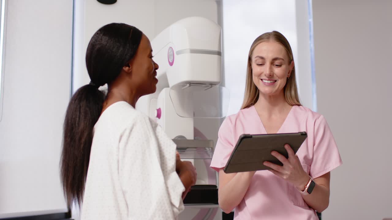 Patient, clinician talking at mammogram, patient asking as clinician tapping tablet confirming plan