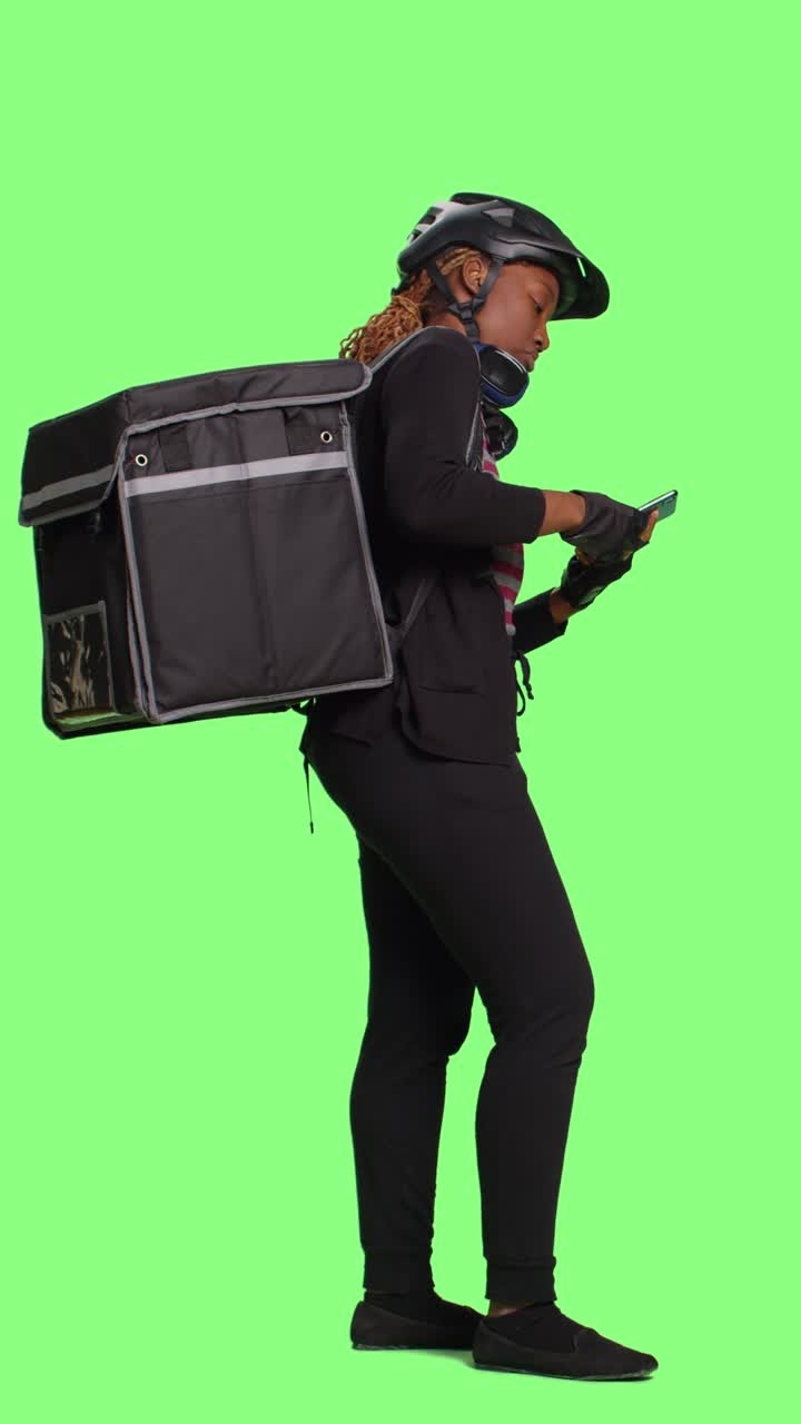 Vertical video: Young takeaway worker delivering food in backpack and browsing internet