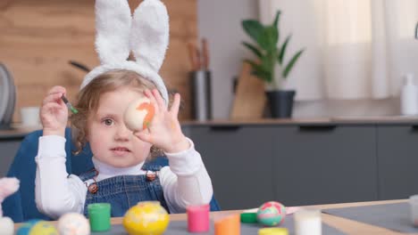 a happy little girl with bunny ears sits in a chair, smiling and gesturing with her fingers, while next to her a flowerpot with a houseplant adds a touch of nature to the scene