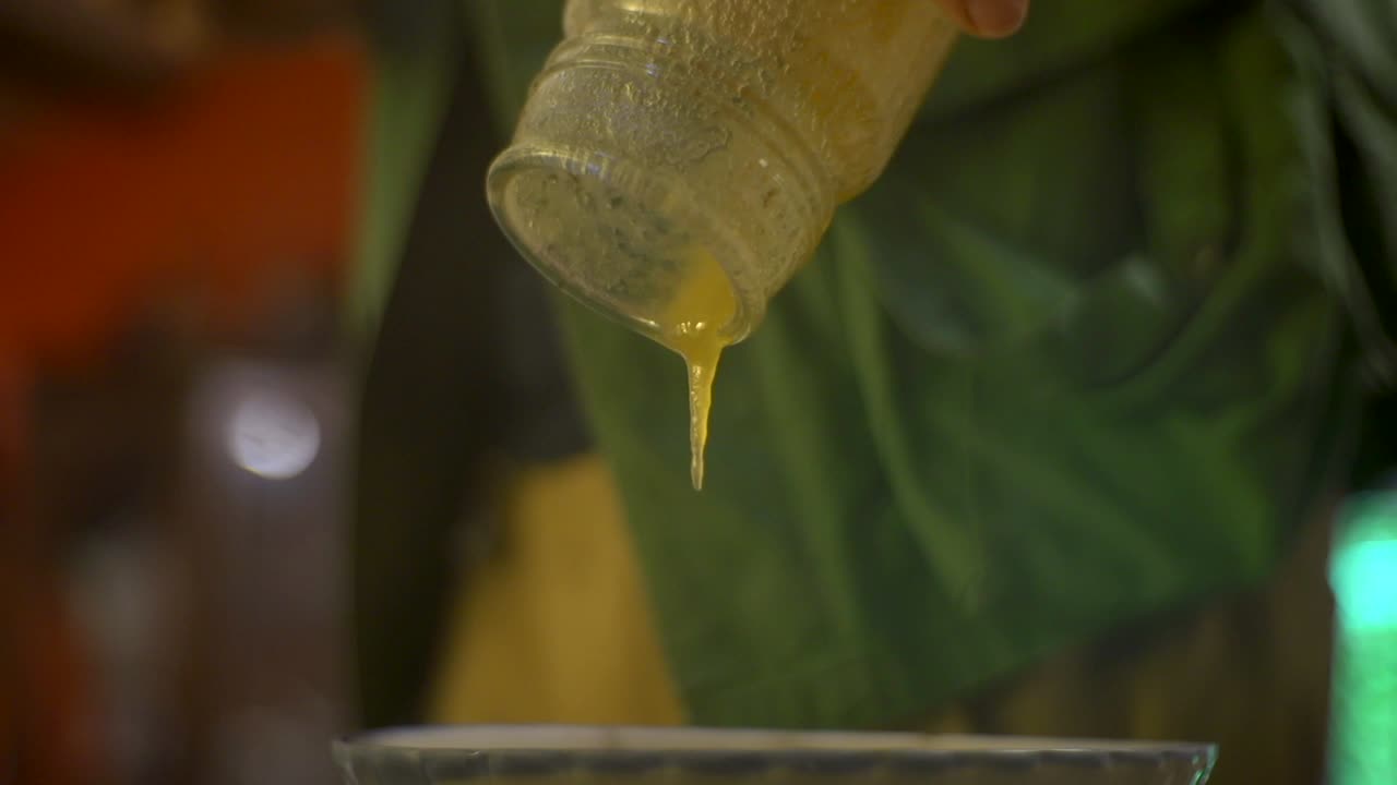 Cold honey in glass jar slowly oozing into bowl, filmed as close up shot