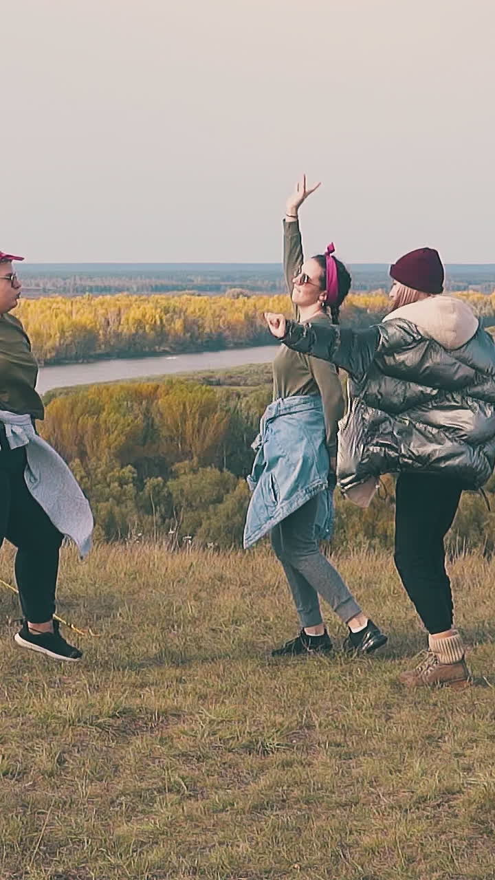 happy young hangover women dance in camp on calm river bank against green and yellow trees in autumn slow motion