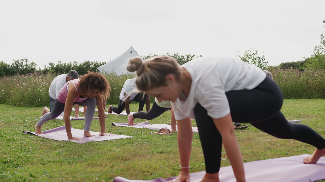 maestra liderando un grupo de hombres y mujeres maduros en clase en un retiro de yoga al aire libre