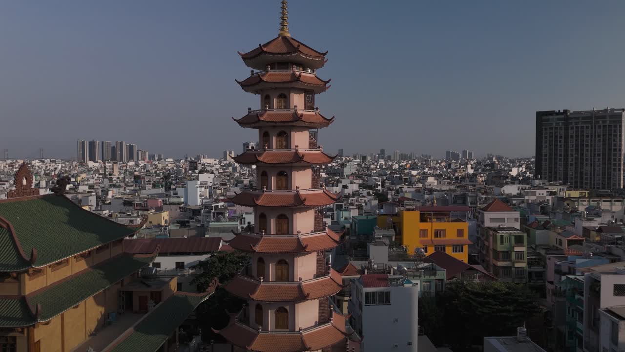 Buddhist Pagoda prayer tower in dense urban area in sunny late afternoon light. Drone camera orbits the structure revealing surrounding area