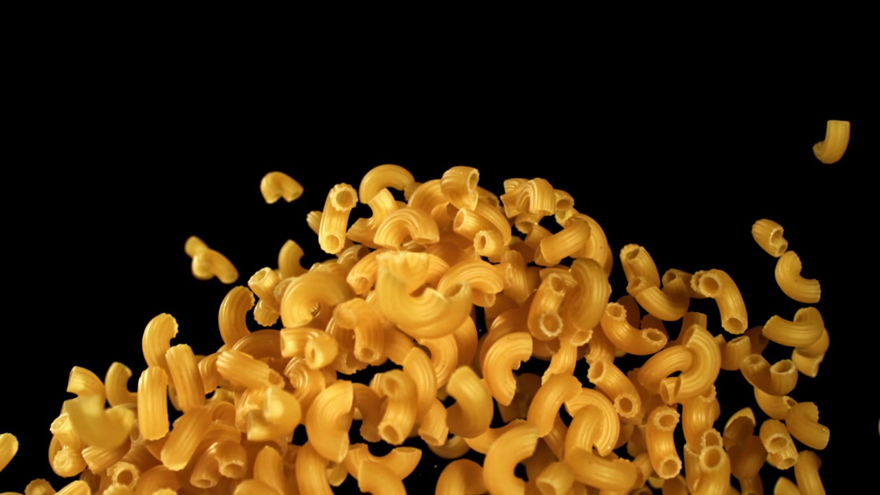 Pasta maccheroni dorata che cade e si accumula su sfondo nero