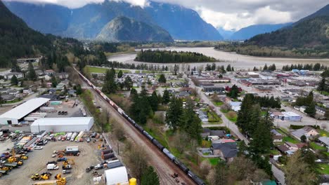 Freight-Train-Passing-By-Industrial-Area-Near-Fraser-River-In-Hope,-British-Columbia,-Canada