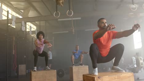 diverse group fitness class jumping onto boxes, cross training at gym, in slow motion