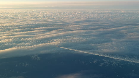 Vista-Increíble-Desde-La-Cabina-De-Un-Avión-Que-Vuela-Alto-Por-Encima-De-Las-Nubes-Dejando-Un-Largo-Rastro-De-Aire-De-Vapor-De-Condensación-Blanco-En-El-Cielo-Azul