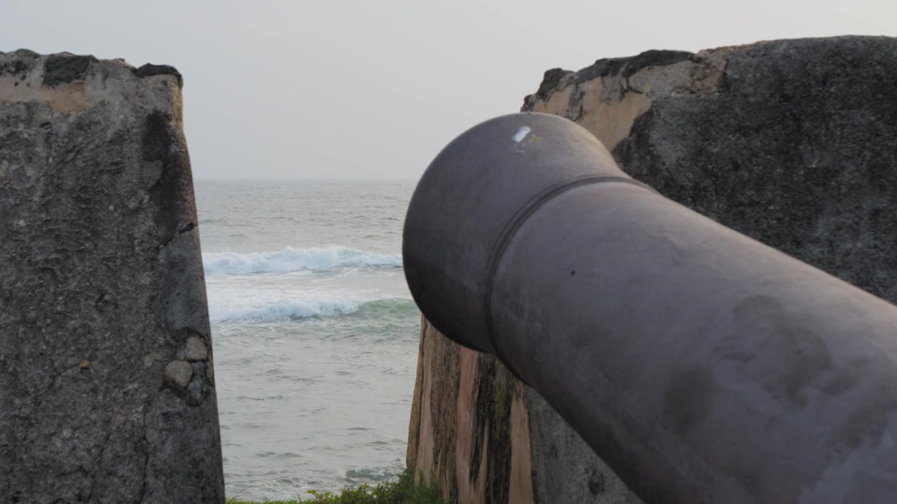 Inquadratura statica ravvicinata di un cannone invecchiato sui bastioni del Forte di Galle, che si affaccia sulle onde dell'Oceano Indiano e sulle antiche mura di pietra sulla costa meridionale dello Sri Lanka