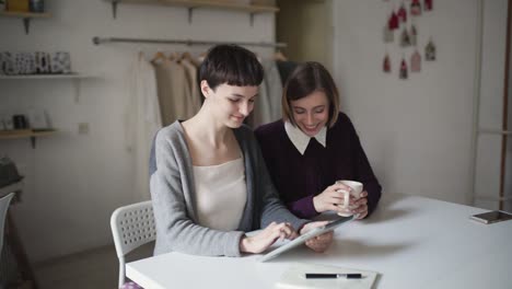 Two-sisters-using-tablet-pc-sitting-at-table-in-home.-Woman-have-fun-with-tablet