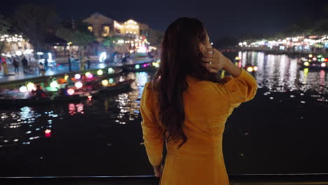 Detrás-De-Una-Foto-De-Una-Mujer-Asiática-Vestida-De-Amarillo-Mirando-Los-Reflejos-Del-Río-Nocturno-En-Hoi-An,-Vietnam