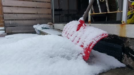 gentle snowflakes fall as a red shovel is covered in heavy snow