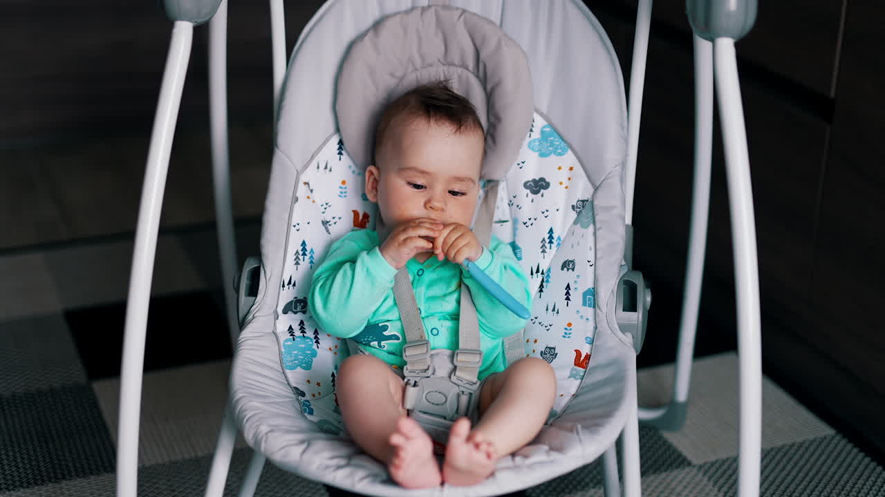 Lovely peaceful child sitting and rocking a in a baby chair. Toddler with dirty face and hands chewing spoon.