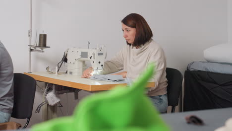 garment makers sewing with machine as they discuss design details, demonstrating collaborative skill in bright workspace, meticulously shaping fabric into finished product, highlighting synergy
