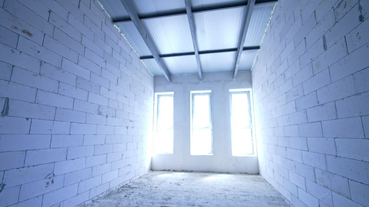 Bright daylight goes into the room through three narrow windows. White brick walls in the room. Construction concept.
