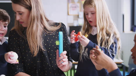 Female-teacher-helping-kids-working-with-construction-blocks-in-a-primary-school-classroom,-close-up