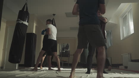 hombre entrena pateando con su pareja sosteniendo la almohadilla en un club deportivo. jóvenes kickboxers golpean la almohada sostenida por el instructor en el gimnasio de lucha en cámara lenta. artes marciales