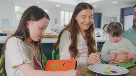 Family-With-Down-Syndrome-Daughter-Sitting-Around-Table-At-Home-Doing-Craft-Making-Card-Together