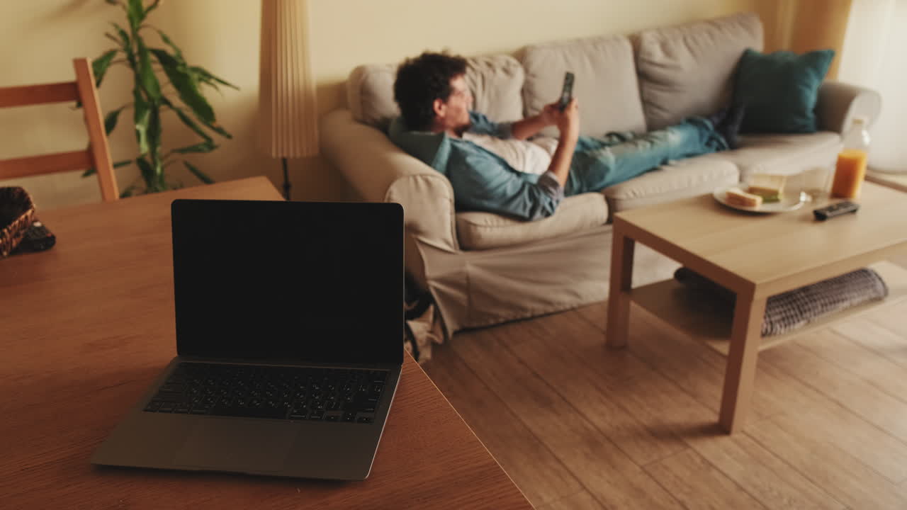 Man relaxing on sofa with laptop and phone in living room