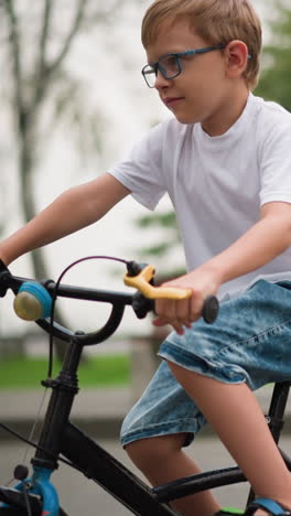 a young boy in a white t-shirt and denim shorts moves his bicycle and rode off, surrounded by greenery, benches, and a calm park environment
