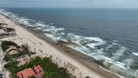 aerial shot of continuous waves approaching the shore of beach with tourists in fortaleza, brazil