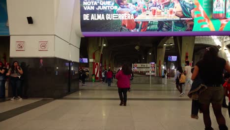 people walk through a bustling station corridor with bright advertisements overhead
