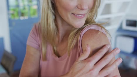 happy caucasian mature woman showing plaster on arm where she was vaccinated against coronavirus