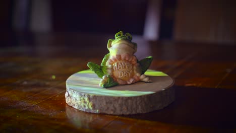 "happy day" written on the frog, close up of a decorative toy frog on a wooden table.material : ceramic